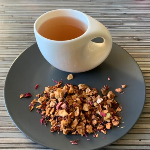 Früchtetee Rhabarberschorle in weißer Tasse aufgegossen und lose auf grauem Teller vor gestreiftem Holzhintergrund