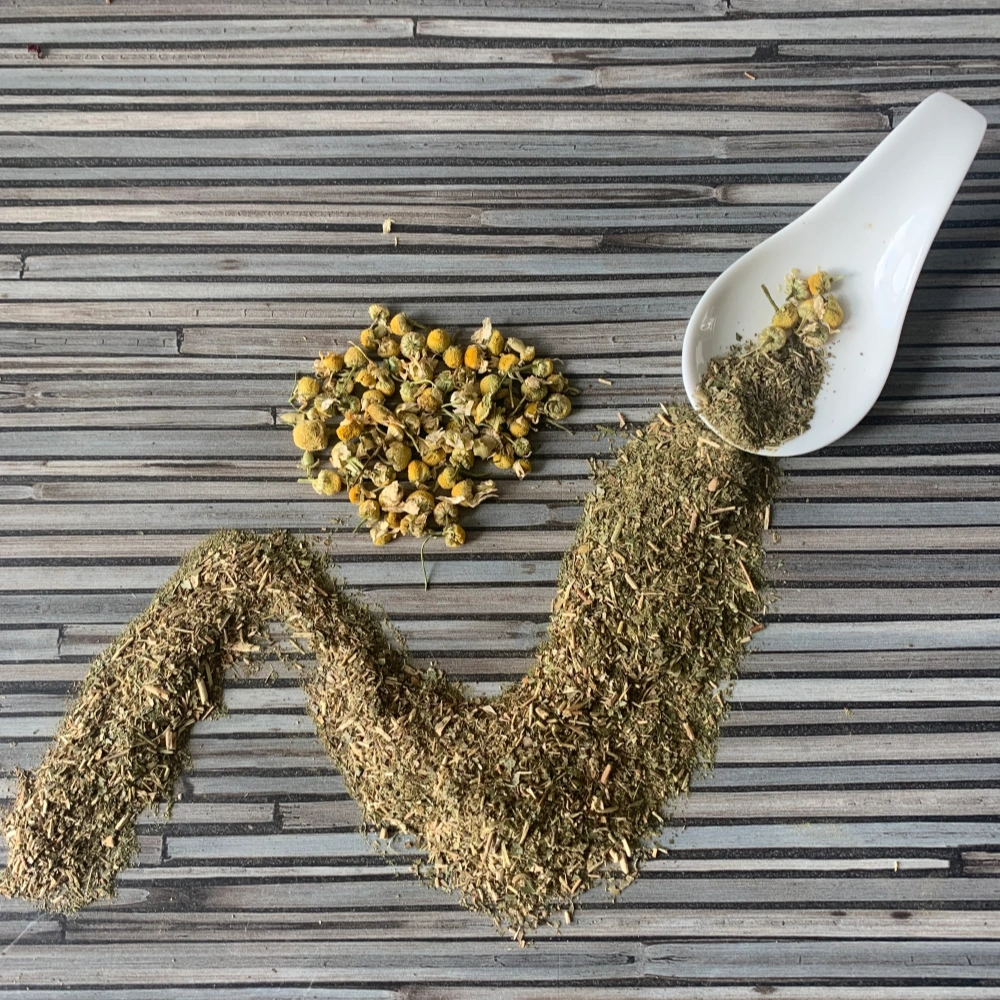 Apoyar mit Kamille mit weißem Porzellanlöffel auf gestreifter Arbeitsplatte.