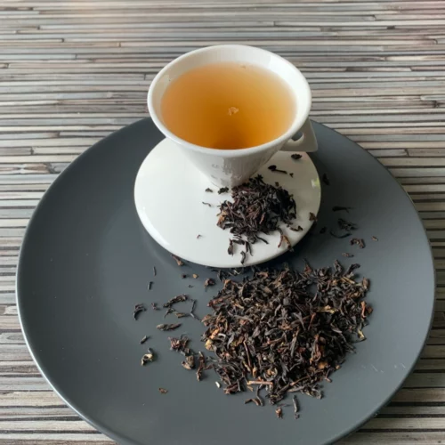 Grauer Teller mit weißer Porzellantasse dunklem Inhalt und Assam Harmutty STGFOP1 lose dekoriert.