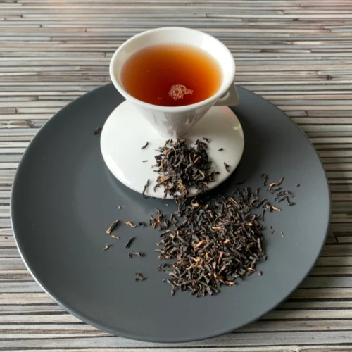 Assam Mangalam FTGFOP1 auf grauem Teller und in weisser Tasse eingeschenkt.