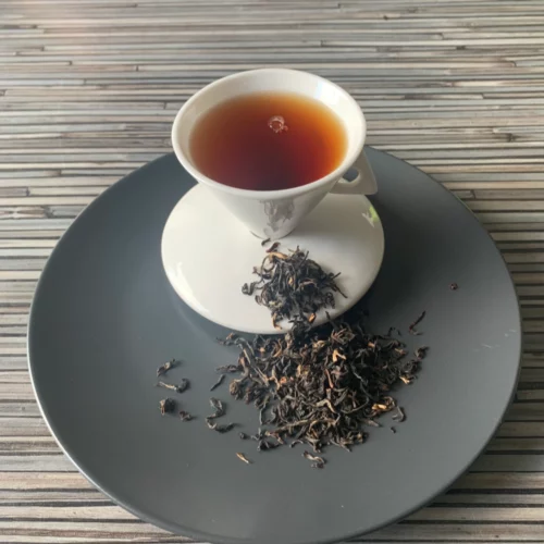 Assam Mokalbari East FTGFOP1 auf grauem Teller und in weisser Tasse eingeschenkt.
