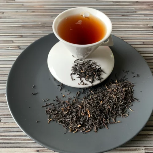 Assam Orangajuli TGFOP auf grauem Teller und in weisser Tasse eingeschenkt.