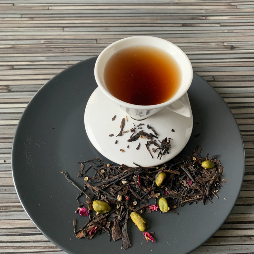 Schwarztee Black Sencha Baklava auf grauem Teller mit weißer Tasse vor gestreiftem Holzhintergrund