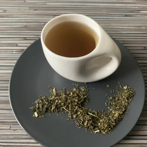 Brennnesselblätter – Brennnesseltee in zart grünlicher Farbe in weißer Tasse, mit getrockneten Brennnesselblättern auf natürlichem Hintergrund