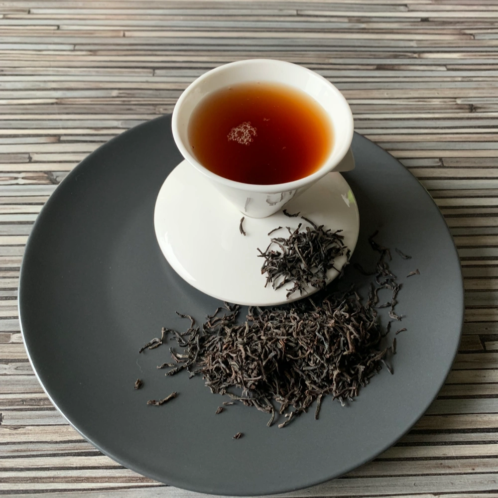 Ceylon Kenilworth OP mit weisser Porzellantasse golden eingeschenkt und lose auf grauem Teller angerichtet.