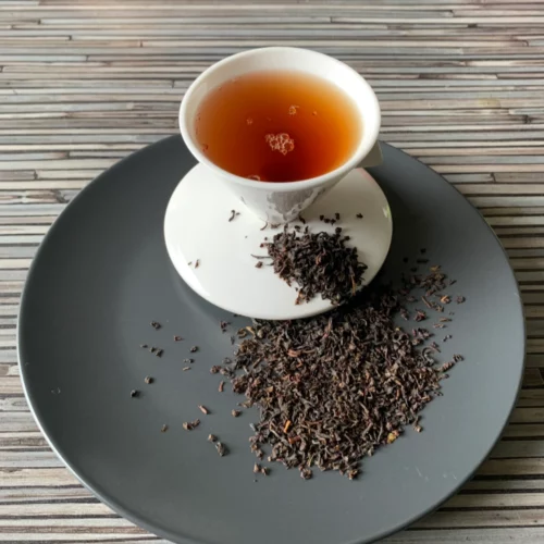 Ceylon Lover's Leap Pekoe mit weisser Porzellantasse golden eingeschenkt und lose auf grauem Teller angerichtet.