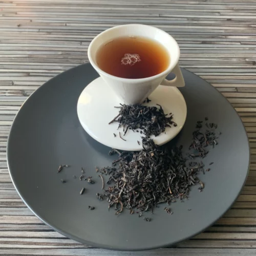 China Lapsang Souchong Schwarztee auf grauem Teller mit weißer Teetasse vor gestreiftem Holz-Hintergrund.