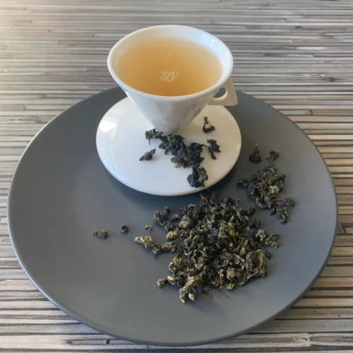 China Milky Oolong Milchtee aromatisiert mit fein gerollten Oolong-Teeblättern und heller, cremiger Tassenfarbe in weißer Teetasse auf gestreiftem Hintergrund