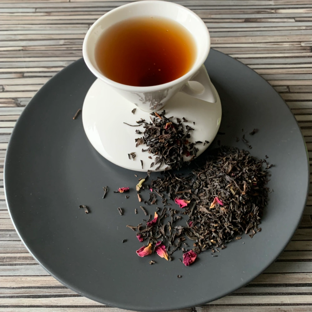 Schwarztee China Rosen Tee OP mit Rosenblüten in weißer Tasse auf grauem Teller vor gestreiftem Holzhintergrund