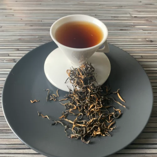 China Special Golden Black Tea auf grauem Teller mit weißer Teetasse vor gestreiftem Holz-Hintergrund