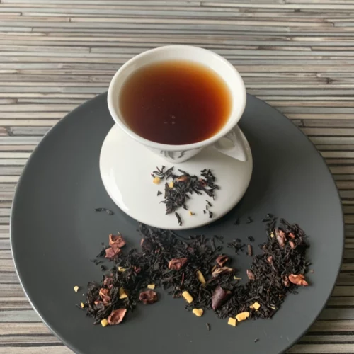 Schwarztee Chocolat mit Kakaostückchen in weißer Tasse auf grauem Teller vor gestreiftem Holzhintergrund