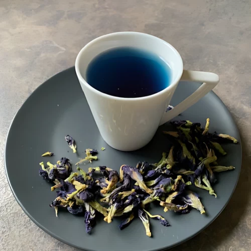 Clitoria ternatea – Butterfly Pea in weiße Tasse, tintenblauer Tee, grauer Teller und loser Clitoria Ternatea Tee auf eleganter Marmorfläche.
