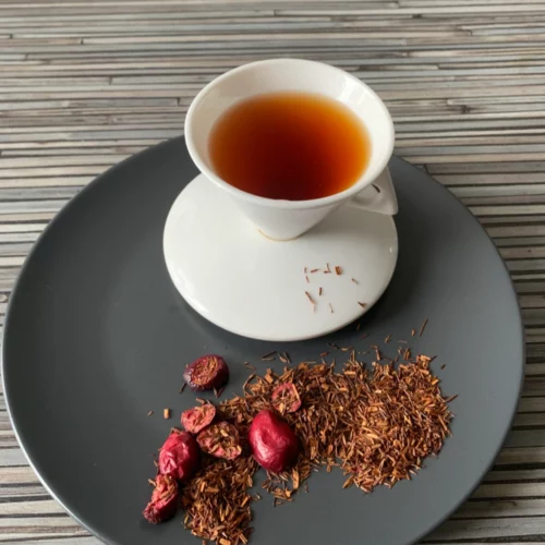 Rotbusch Cranberry Vanille in weißer Tasse, lose Teemischung mit Cranberryscheiben im Teller auf gestreiftem Untergrund