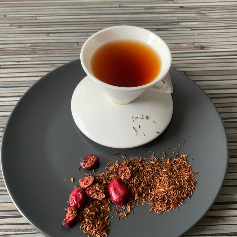 Rotbusch Cranberry Vanille in weißer Tasse, lose Teemischung mit Cranberryscheiben im Teller auf gestreiftem Untergrund