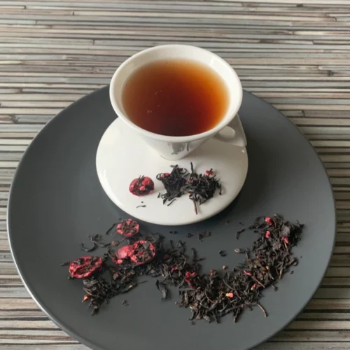 Schwarztee Crannyberry mit Beerenstücken in weißer Tasse auf grauem Teller vor gestreiftem Holzhintergrund