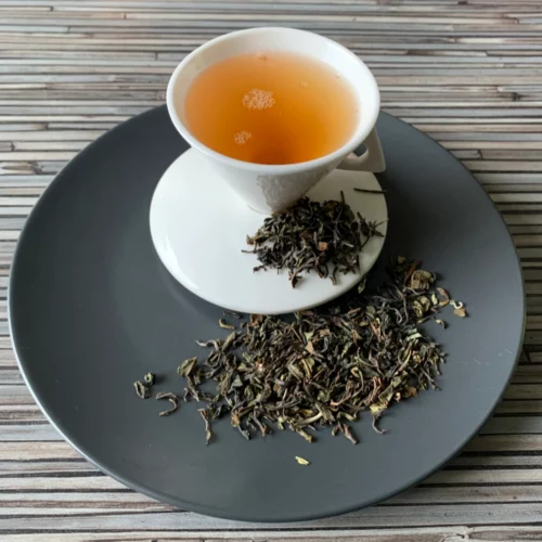 Schwarztee Darjeeling Lingia TGFOP auf grauem Teller mit weißer Tasse vor gestreiftem Holzhintergrund
