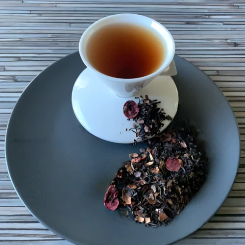 Schwarztee Donna Mirtillo mit Beeren und Kakaostücken in weißer Tasse auf grauem Teller vor gestreiftem Holzhintergrund