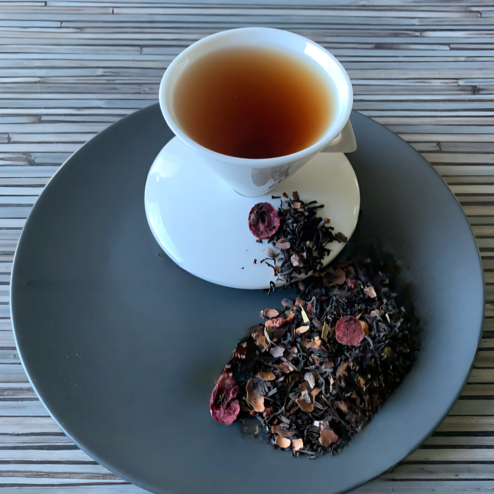 Schwarztee Donna Mirtillo mit Beeren und Kakaostücken in weißer Tasse auf grauem Teller vor gestreiftem Holzhintergrund