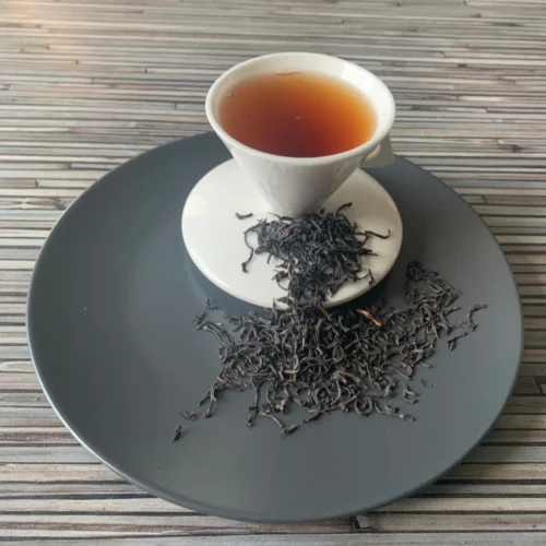 Englische Blatt-Mischung auf grauem Teller mit weißer Tasse vor gestreiftem Holzhintergrund