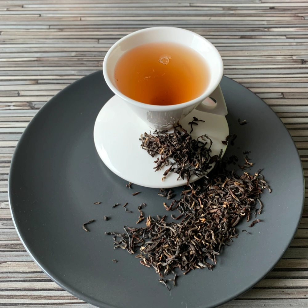 Nepal Maloom FTGFOP2 auf grauem Teller mit weißer Tasse vor gestreiftem Holzhintergrund