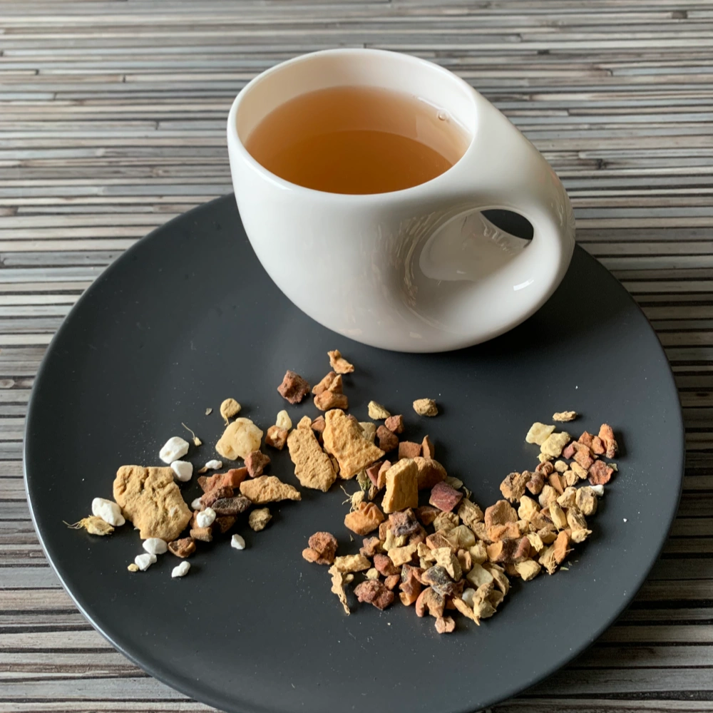 Früchtetee Ingwer Basilikum Zitrone in weißer Tasse auf grauem Teller vor gestreiftem Holzhintergrund