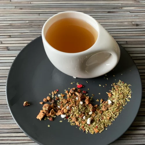 Früchtetee Mate Granate in weißer Tasse aufgegossen und lose auf grauem Teller vor gestreiftem Holzhintergrund