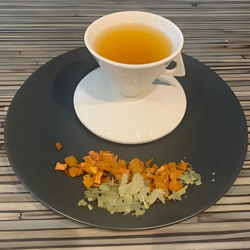 Früchtetee Anabama Mangoblätter in weißer Tasse auf grauem Teller vor gestreiftem Holzhintergrund