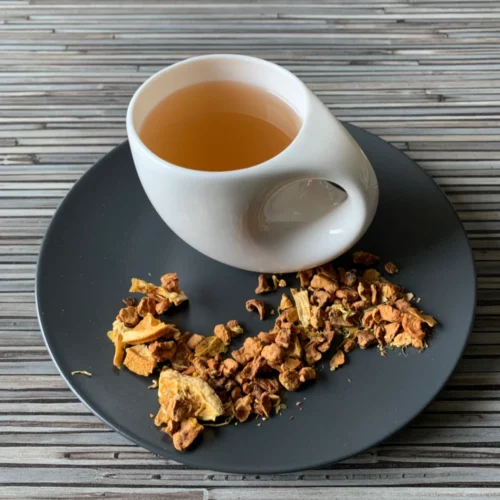 Früchtetee Apfelsinentraum Apfelsinen Note in weißer Tasse auf grauem Teller vor gestreiftem Holzhintergrund