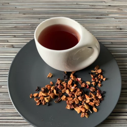 Früchtetee Blauer Granatapfel in weißer Tasse auf grauem Teller vor gestreiftem Holzhintergrund