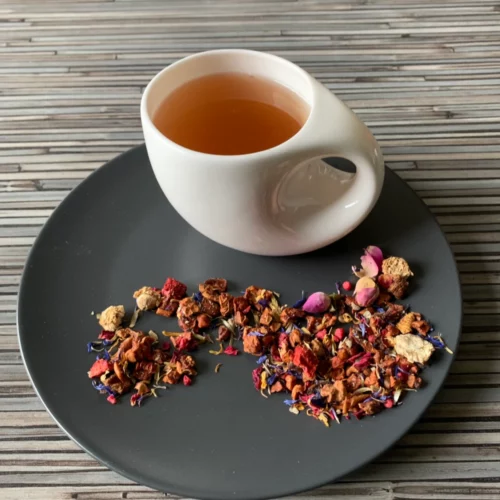 Früchtetee Blumengarten Erdbeer in weißer Tasse auf grauem Teller vor gestreiftem Holzhintergrund