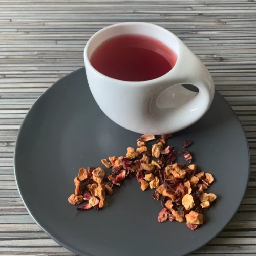 Früchtetee Blutorange in weißer Tasse auf grauem Teller vor gestreiftem Holzhintergrund