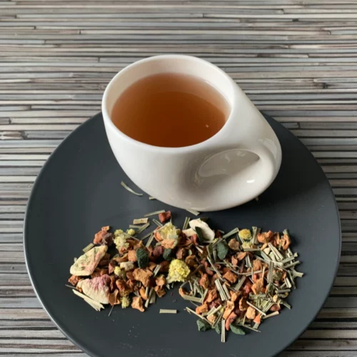 Früchtetee Cranberry Feige Spirulina in weißer Tasse auf grauem Teller vor gestreiftem Holzhintergrund