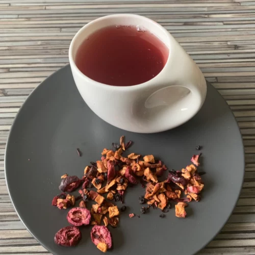 Früchtetee Cranberry Vanille in weißer Tasse auf grauem Teller vor gestreiftem Holzhintergrund