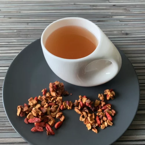 Früchtetee Goji Beerchen in weißer Tasse auf grauem Teller vor gestreiftem Holzhintergrund
