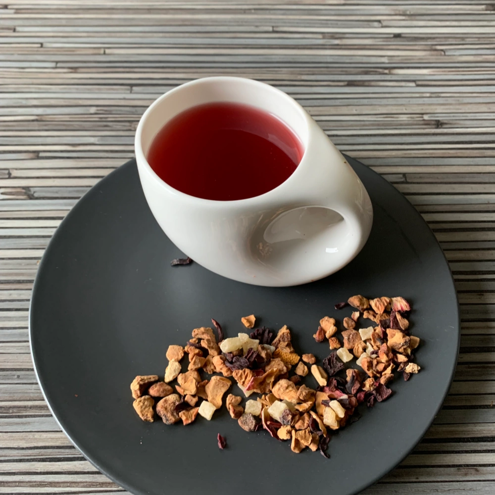 Früchtetee Gute Laune in weißer Tasse auf grauem Teller vor gestreiftem Holzhintergrund