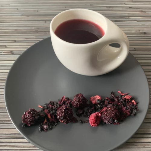 Früchtetee Jamaika Rum in weißer Tasse auf grauem Teller vor gestreiftem Holzhintergrund