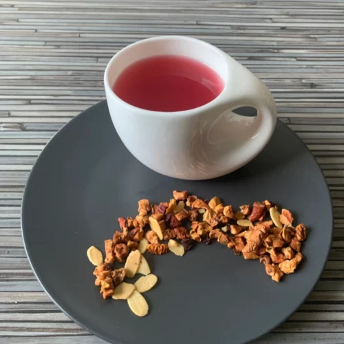 Früchtetee Kirmes Mandel in weißer Tasse auf grauem Teller vor gestreiftem Holzhintergrund