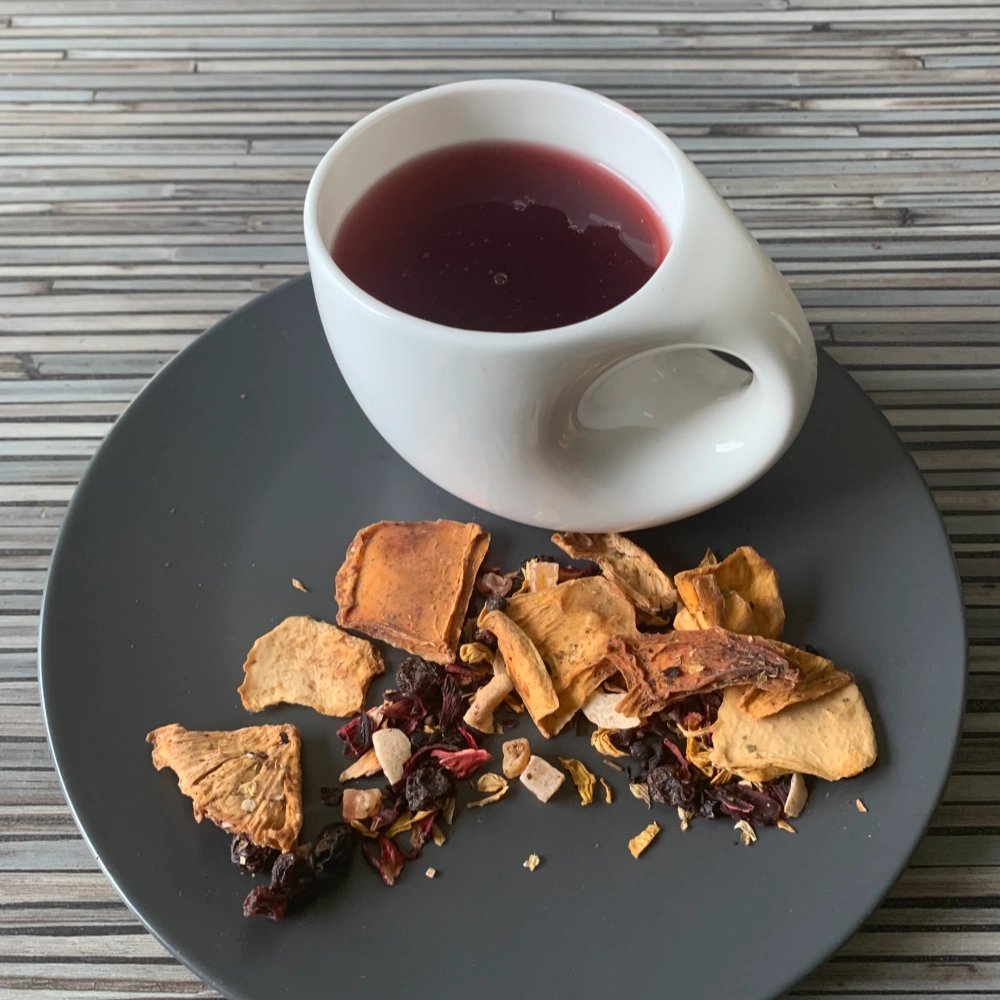 Früchtetee Mango Joghurt in weißer Tasse aufgegossen und lose auf grauem Teller vor gestreiftem Holzhintergrund