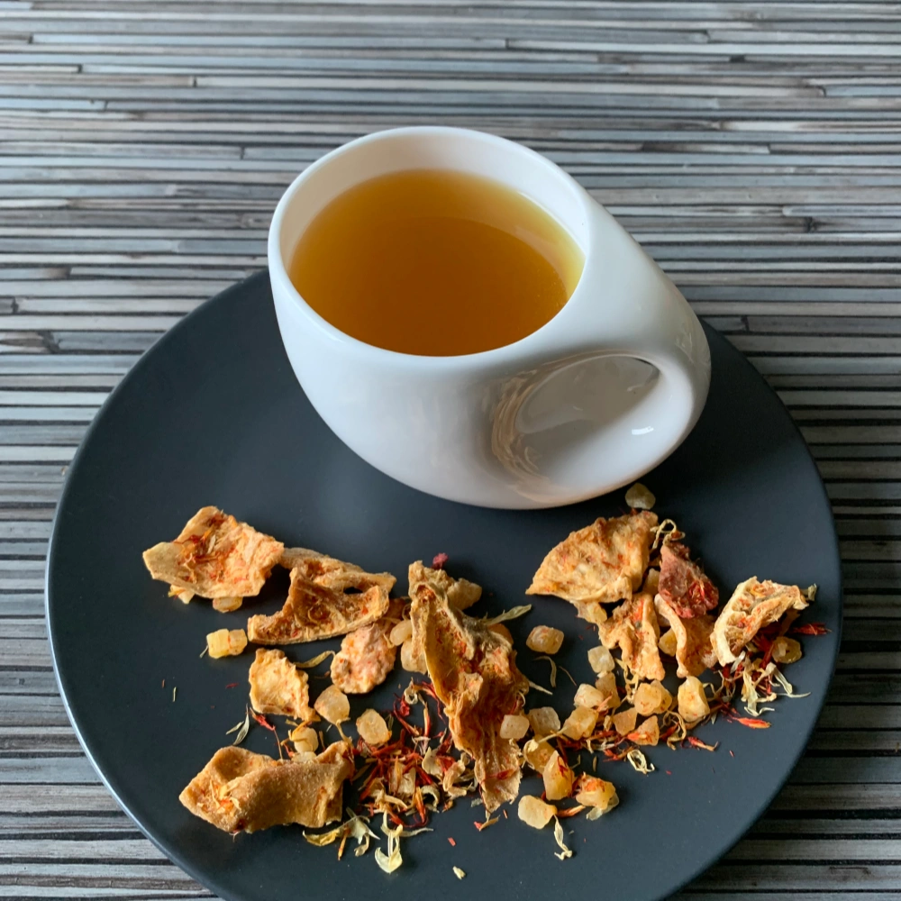 Früchtetee Mango ’n Friends in weißer Tasse auf grauem Teller vor gestreiftem Holzhintergrund