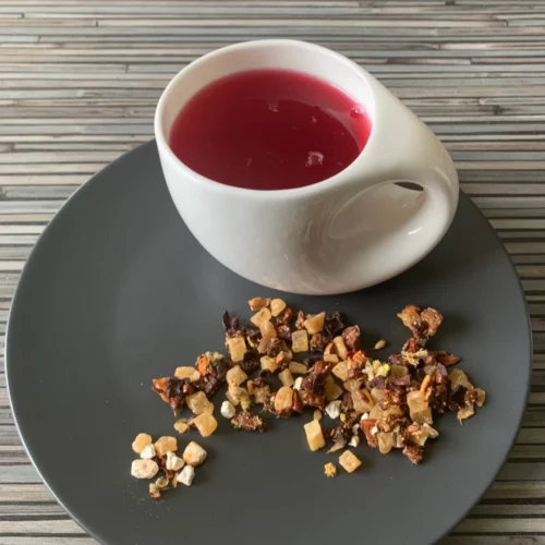 Früchtetee Süße Rhabarberlimo in weißer Tasse aufgegossen und lose auf grauem Teller vor gestreiftem Holzhintergrund