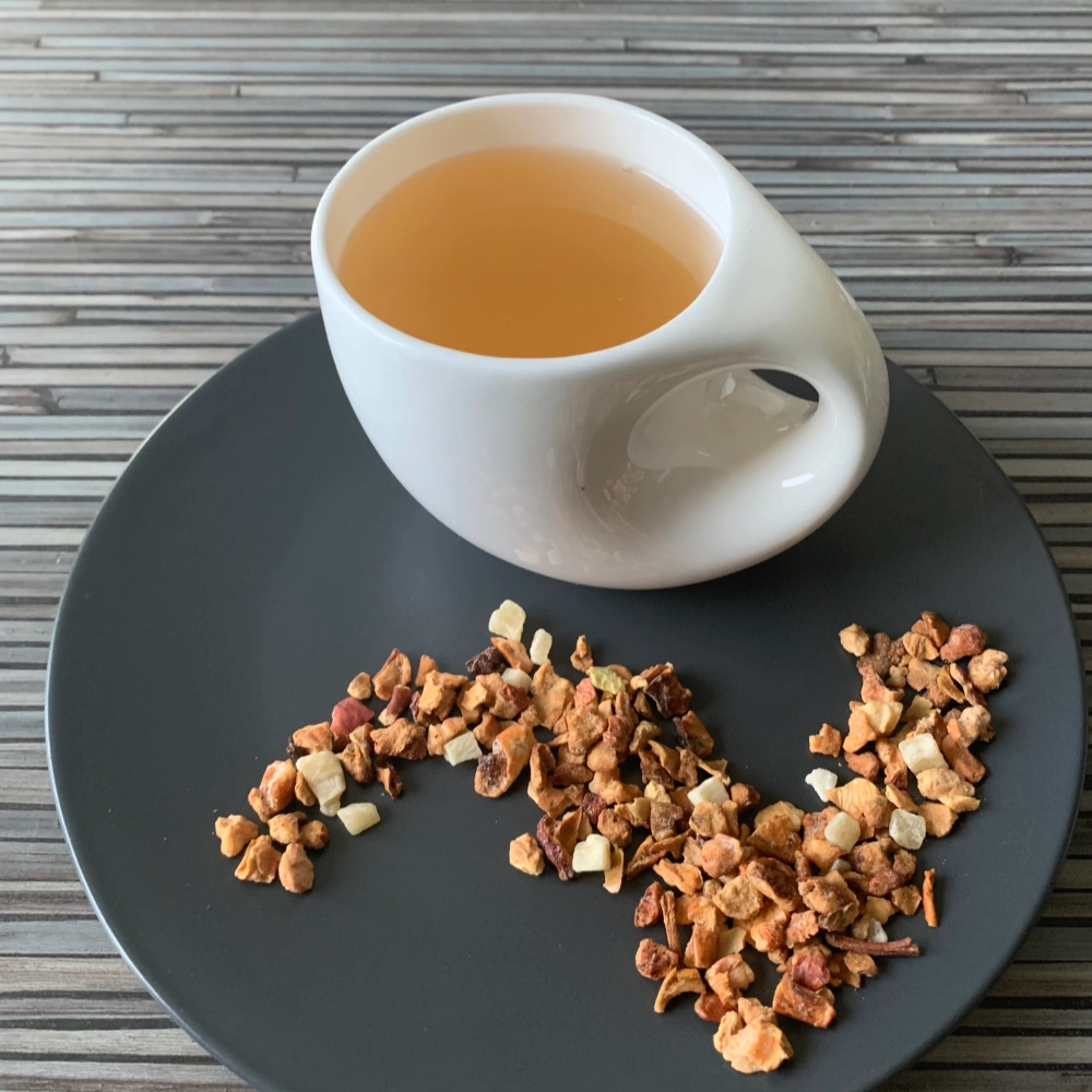 Früchtetee Türkischer Apfeltee in weißer Tasse aufgegossen und lose auf grauem Teller vor gestreiftem Holzhintergrund