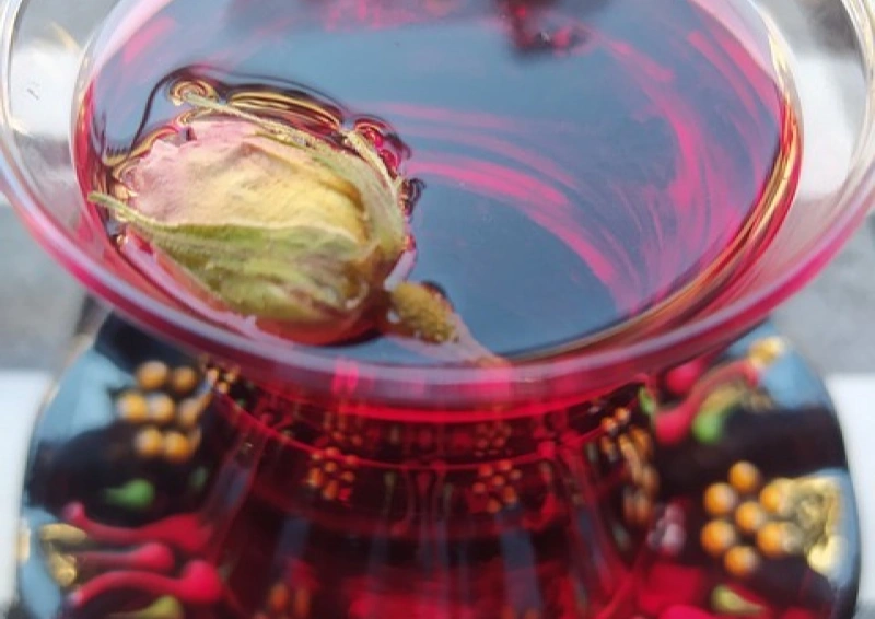 Früchtetees, hier ein Roter mit Rosenknospe im Glas schwimmend.