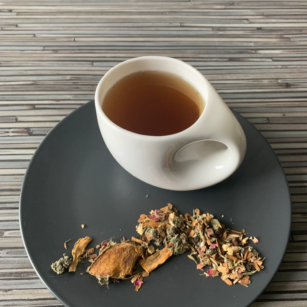 Gewürztee Harmonie der 7 Chakren in weißer Teetasse, lose Gewürzteemischung mit Blüten und Gewürzen auf gestreiftem Holzuntergrund