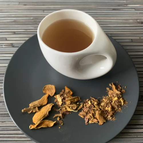 Gewürztee Kurkuma Relax ohne Aromazusätze in weißer Tasse auf dunklem Teller auf gestreifter Holzplatte, loser Kurkuma-Gewürztee daneben