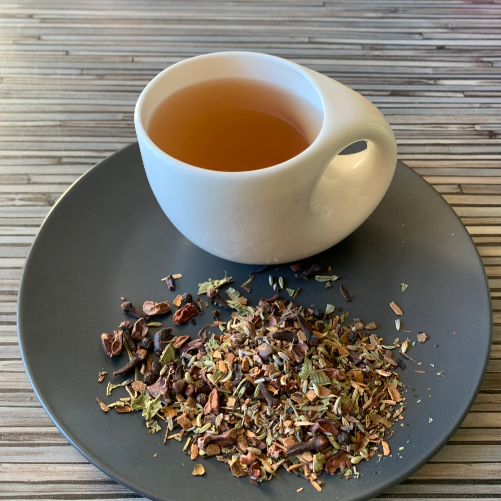 Gewürztee Schoko Chai ohne Zusätze in dunkler Tasse, lose Teemischung mit Kakao, Gewürzen und Lavendel auf Holzuntergrund