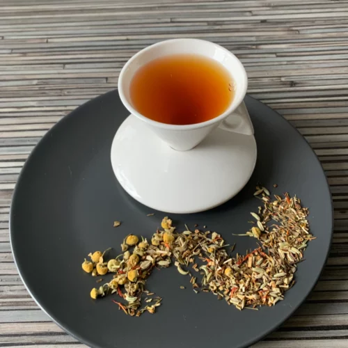 Grüner Honeybusch-Rotbusch Entspannungszeittee mit grünem Honeybusch und Kamillenblüten und heller, kupferner Tassenfarbe in weißer Teetasse auf gestreiftem Hintergrund