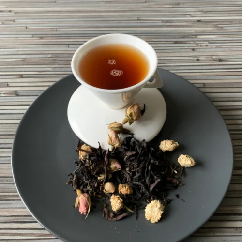 Grüner Oolong Blume Asiens halbfermentierter Tee mit Teeblättern, Rosenknospen und Kamillenblüten und heller, klarer Tassenfarbe in weißer Teetasse auf gestreiftem Hintergrund