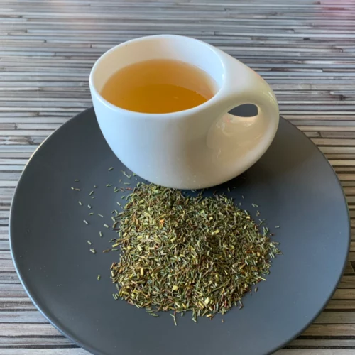 Grüner Rotbuschtee pur mit grünen Rooibos-Teeblättern und heller, goldgelber Tassenfarbe in weißer Teetasse auf gestreiftem Hintergrund
