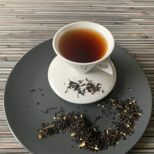 Schwarztee Irish Morning mit Kokosraspeln und Blüten in weißer Tasse auf grauem Teller vor gestreiftem Holzhintergrund