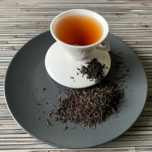 Schwarzer Tee Japan Benifuuki auf grauem Teller mit weißer Tasse vor gestreiftem Holzhintergrund